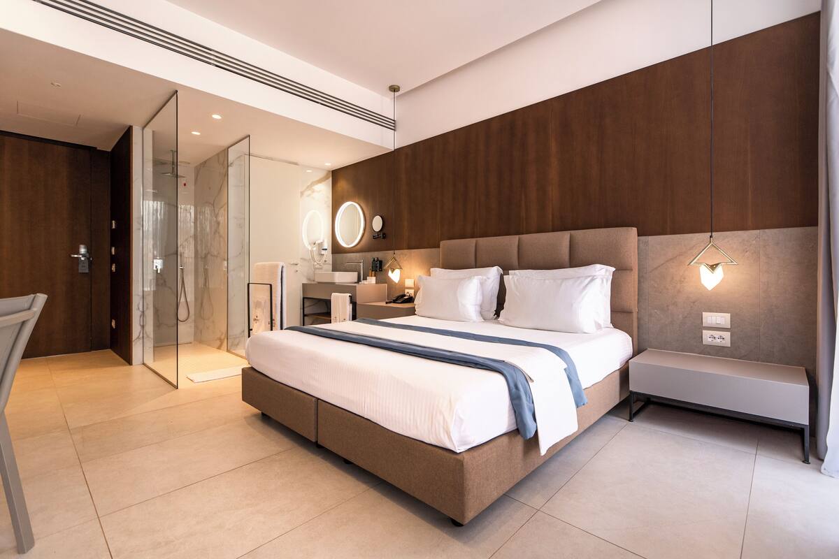 Una habitación de hotel moderna con una cama grande, una mesita de noche, un espejo y un banco.