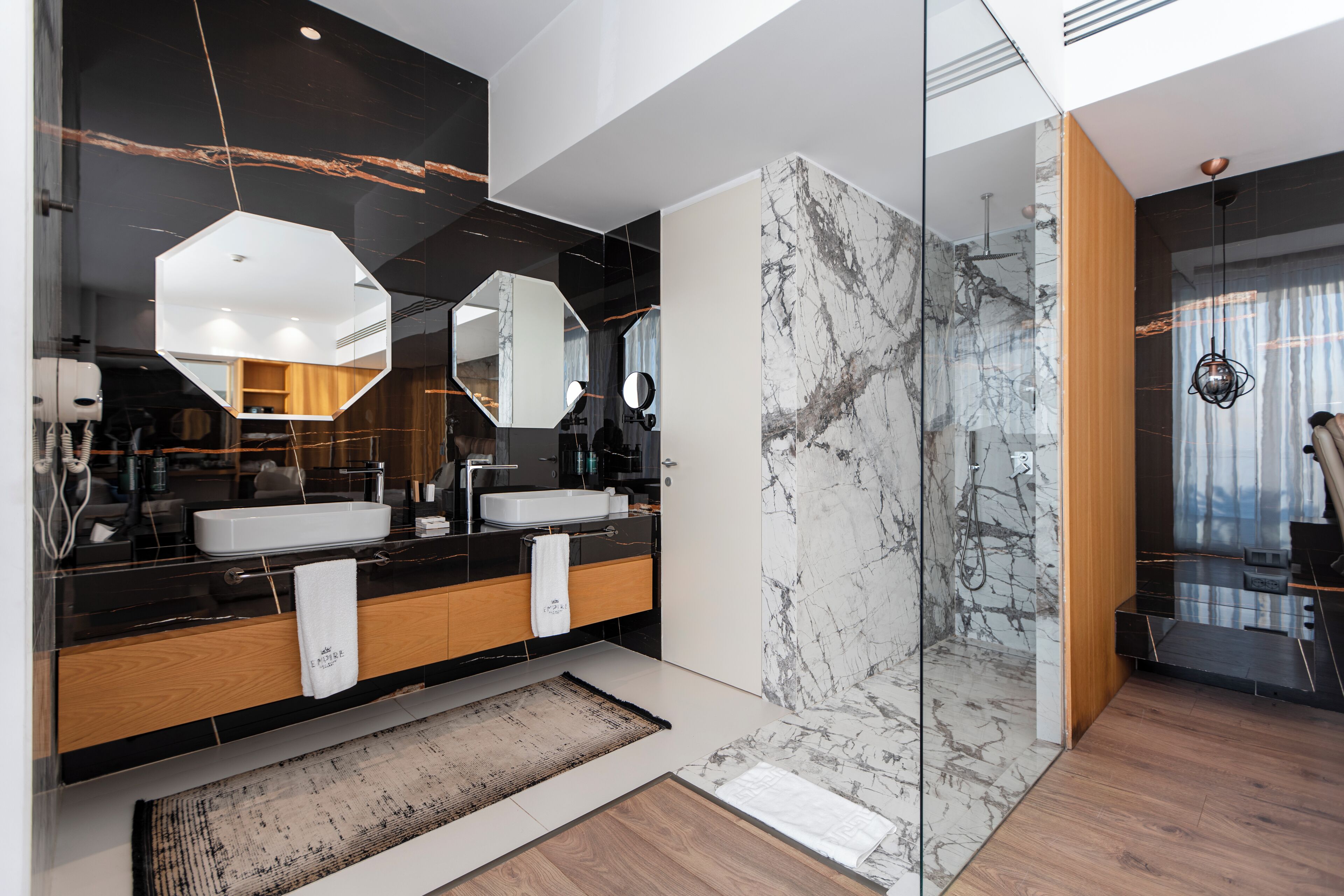 A modern bathroom with a large mirror, two sinks, and a marble shower wall.