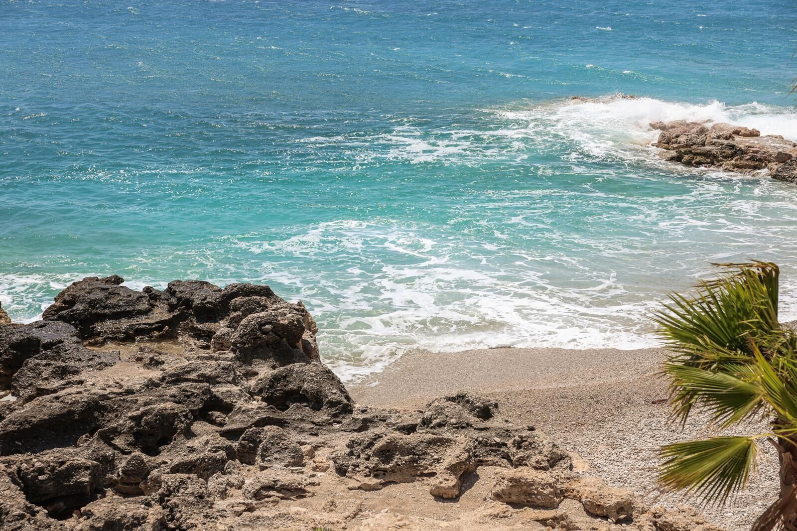A rocky shoreline with clear turquoise water and waves crashing onto the beach.