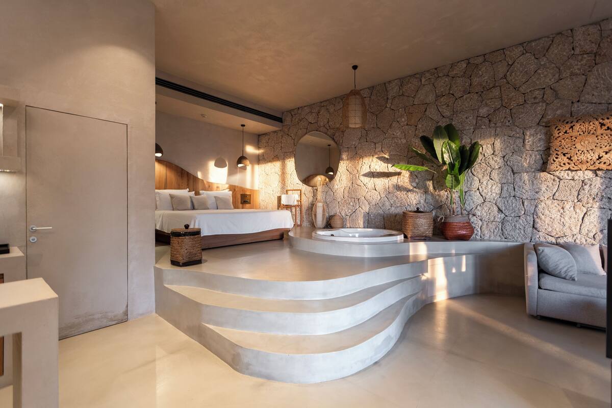Un baño moderno con pared de piedra, una bañera independiente y un espejo grande.