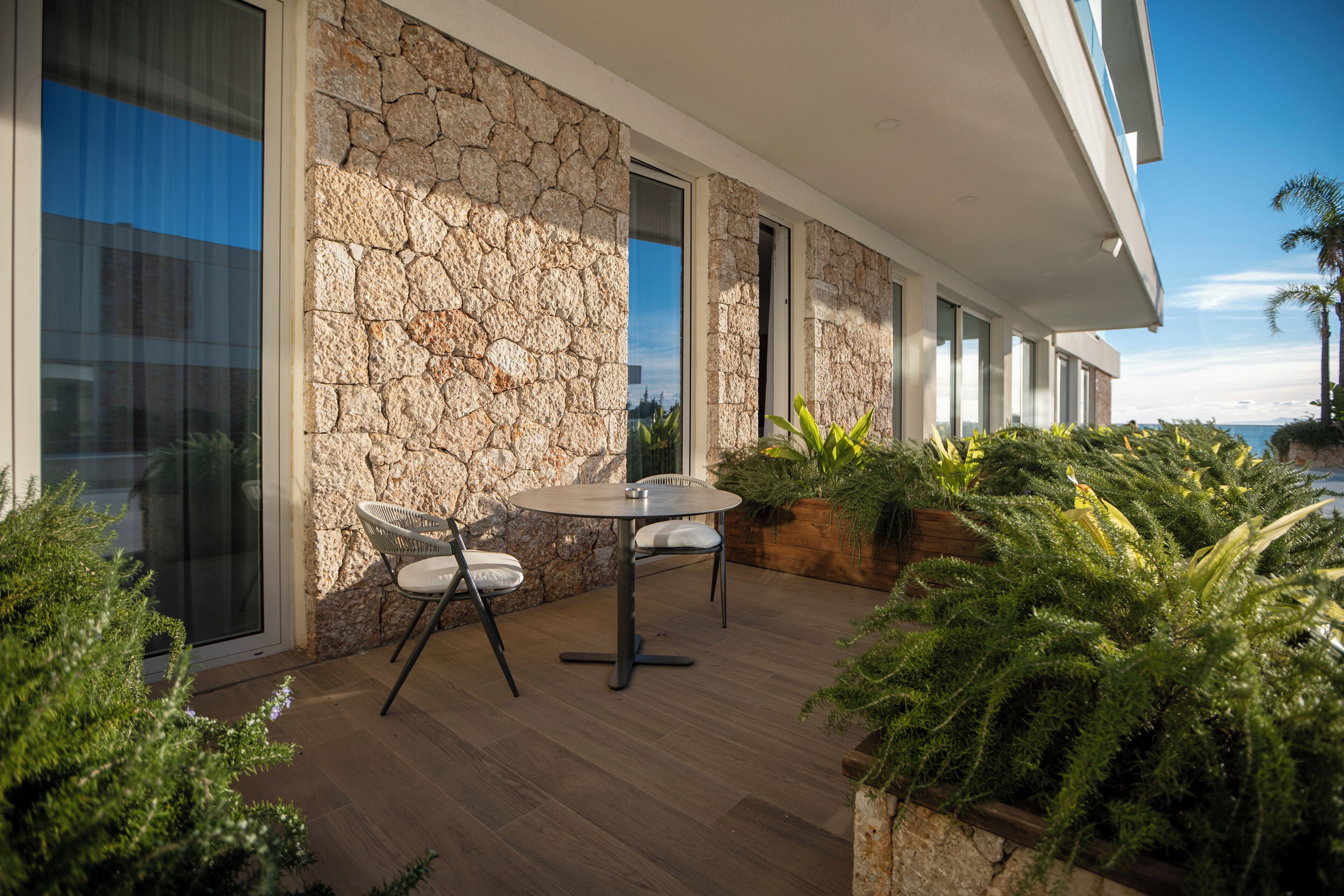 Une terrasse extérieure moderne, agrémentée d’un mur en pierre, d’une table ronde avec des chaises et d’une végétation luxuriante.