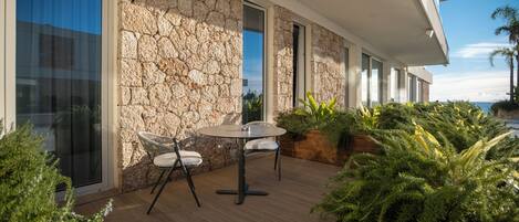 Une terrasse extérieure moderne, agrémentée d’un mur en pierre, d’une table ronde avec des chaises et d’une végétation luxuriante.