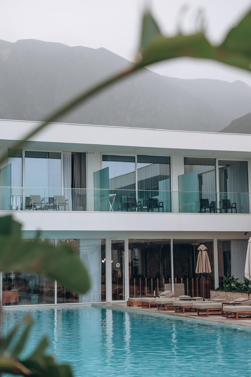 A modern two-story building with a swimming pool, glass railings, and outdoor seating.