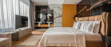 A modern bedroom with a large bed, a TV, a vanity, and a bathroom in the background.