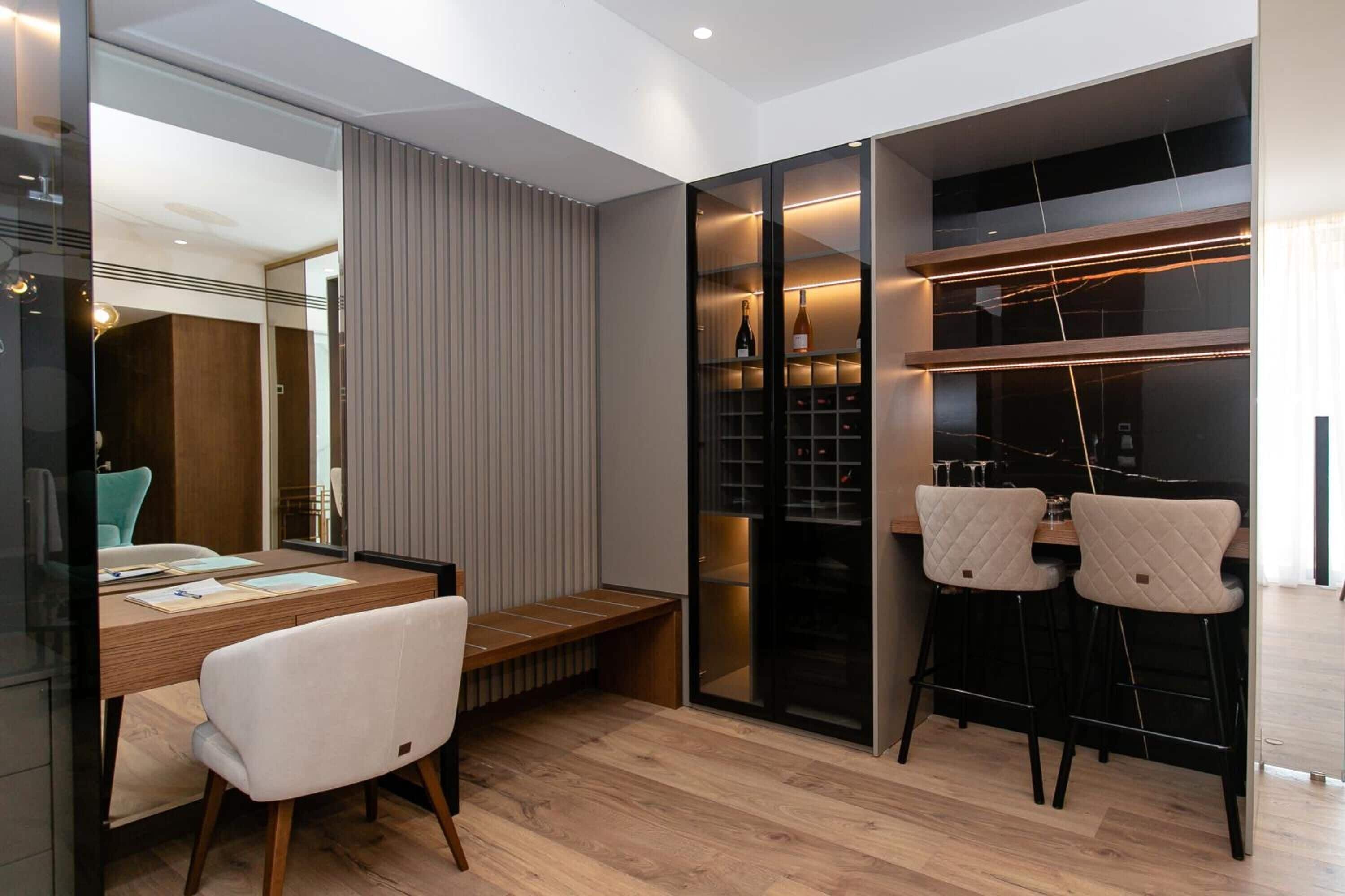 A modern dining area with a wooden table, two white chairs, a bench, and a wine rack with bottles.