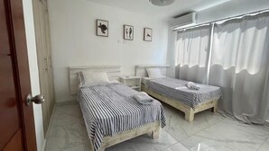 Una habitación con dos camas, ventilador de techo y ventana con cortinas.