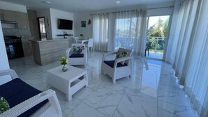 Una sala de estar moderna con muebles de mimbre blanco, una cocina con estufa y un balcón con cortinas.