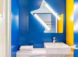 Un baño con un lavamanos blanco, un espejo de forma original y una toalla sobre la encimera.