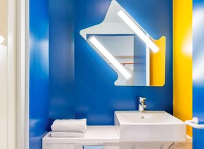 Un baño con un lavamanos blanco, un espejo de forma original y una toalla sobre la encimera.