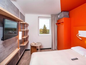 Una habitación de hotel moderna con cama, televisión montada en la pared, una mesita y una ventana con cortinas.