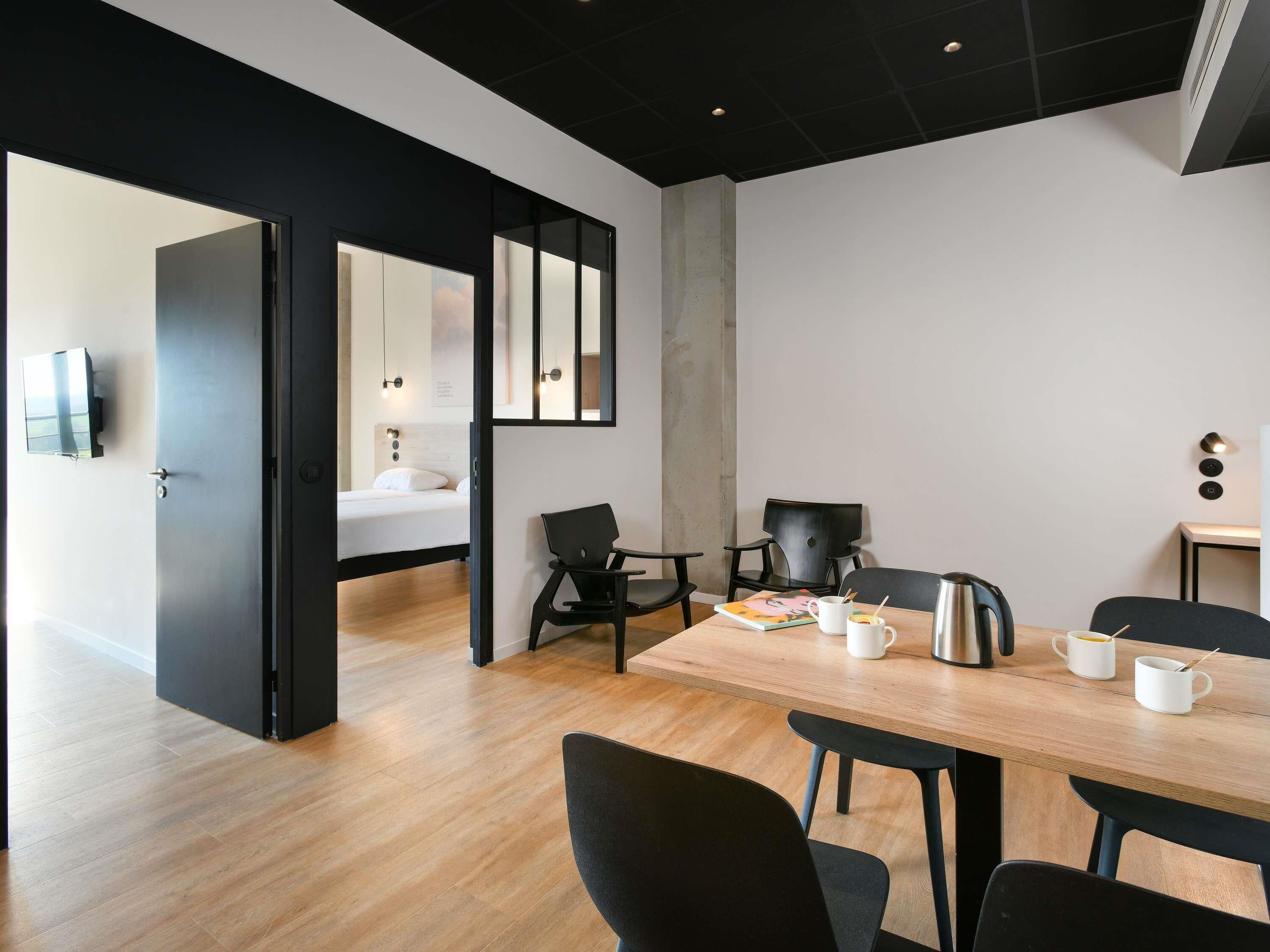 A modern hotel room with a wooden floor, a bed with white bedding, a desk with a chair, and a coffee table.