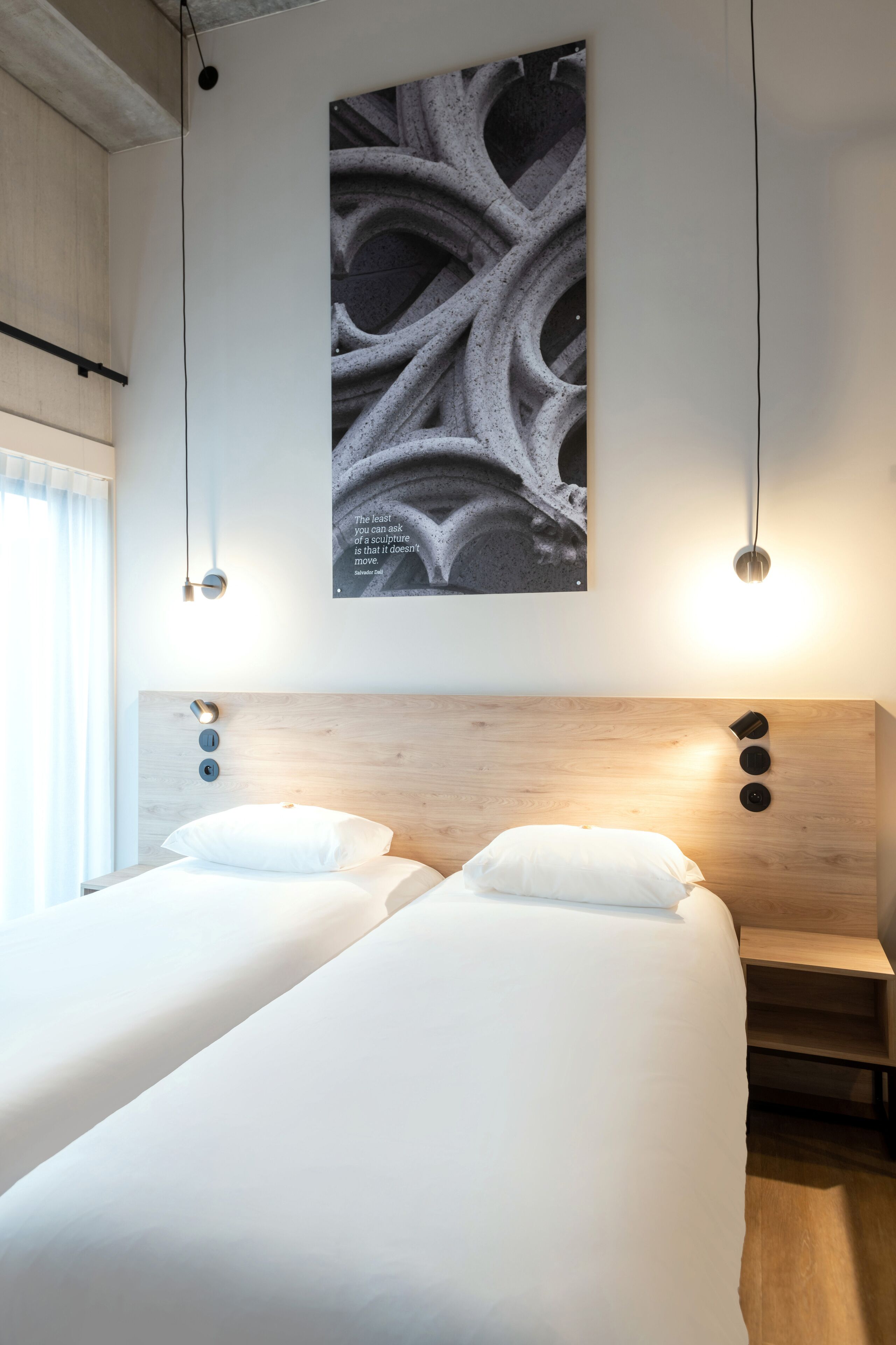 Een hotelkamer met twee bedden, een houten hoofdbord, een kunstwerk aan de muur en hanglampen.