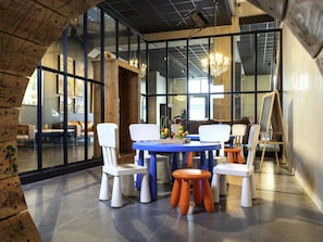 A modern interior with a round table, white and orange chairs, and a large window. - Ibis Styles Namur (Namur)