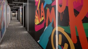 A hallway with a colorful mural on the wall, a carpeted floor, and a series of doors on the left. - Ibis Styles Namur (Namur)