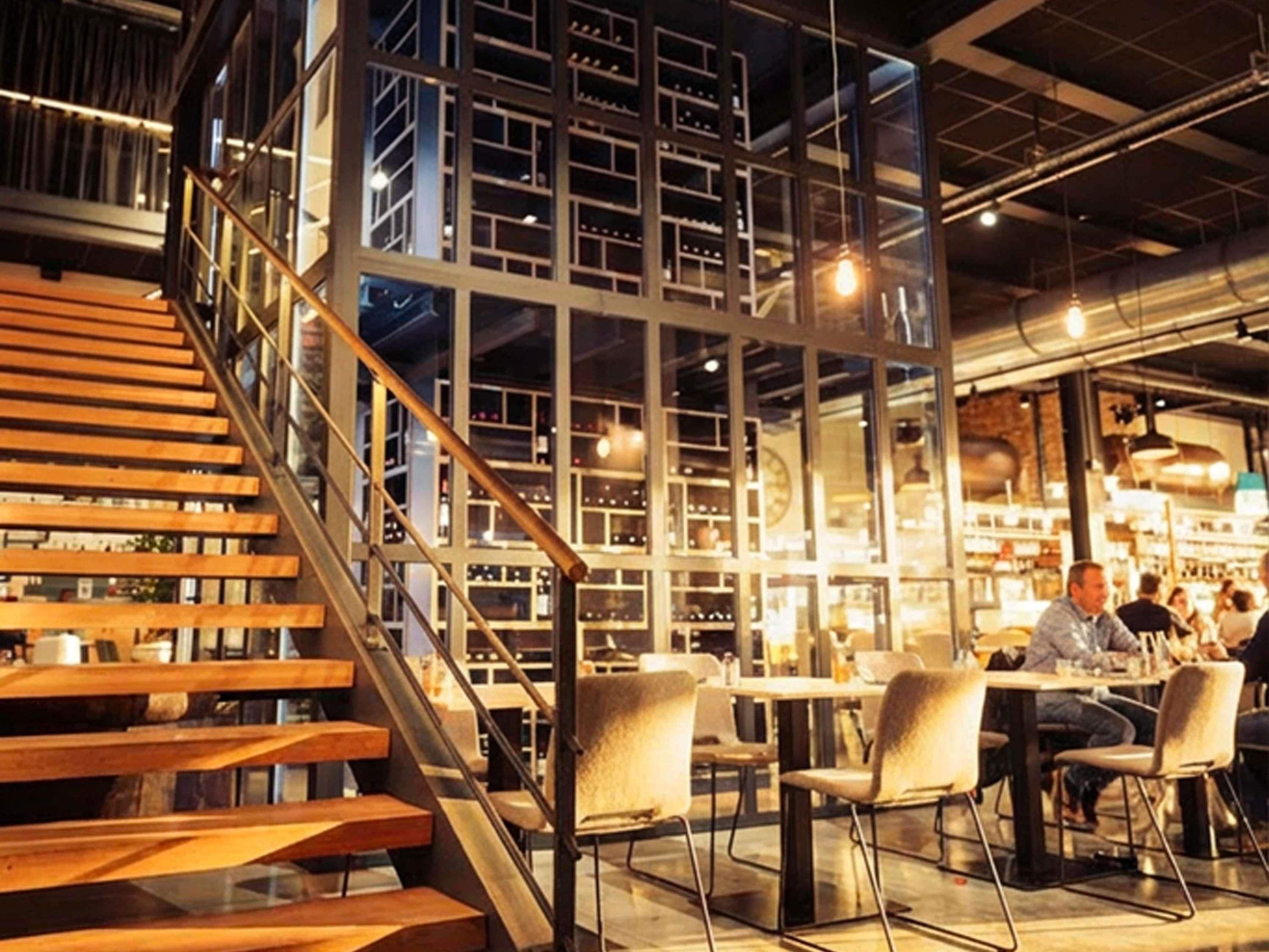 Un intérieur moderne avec un escalier menant à une mezzanine, qui comprend un espace repas avec des tables et des chaises.