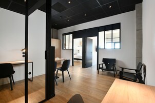 Un espacio de oficina moderno con suelo de madera, sillas negras, un escritorio y ventanas amplias que dejan entrar luz natural.