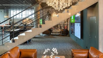 A spacious lobby with a chandelier, leather sofas, a wooden coffee table with orchids, and a staircase.