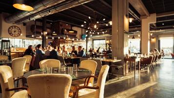 An indoor dining area with tables and chairs, a clock on the wall, and a view of the outside through large windows.