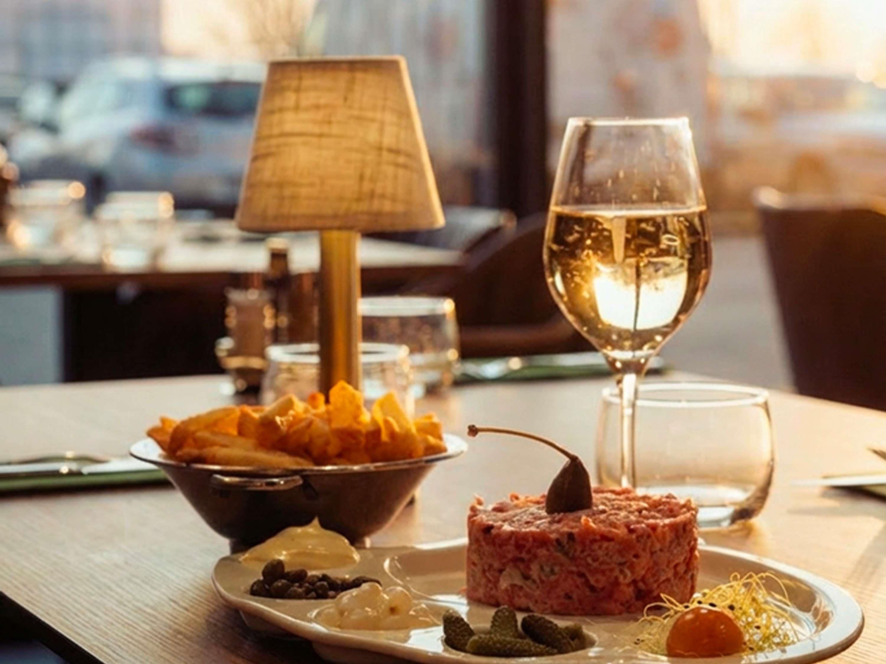 Una mesa de comedor con un plato de comida, una copa de vino blanco y una lámpara.