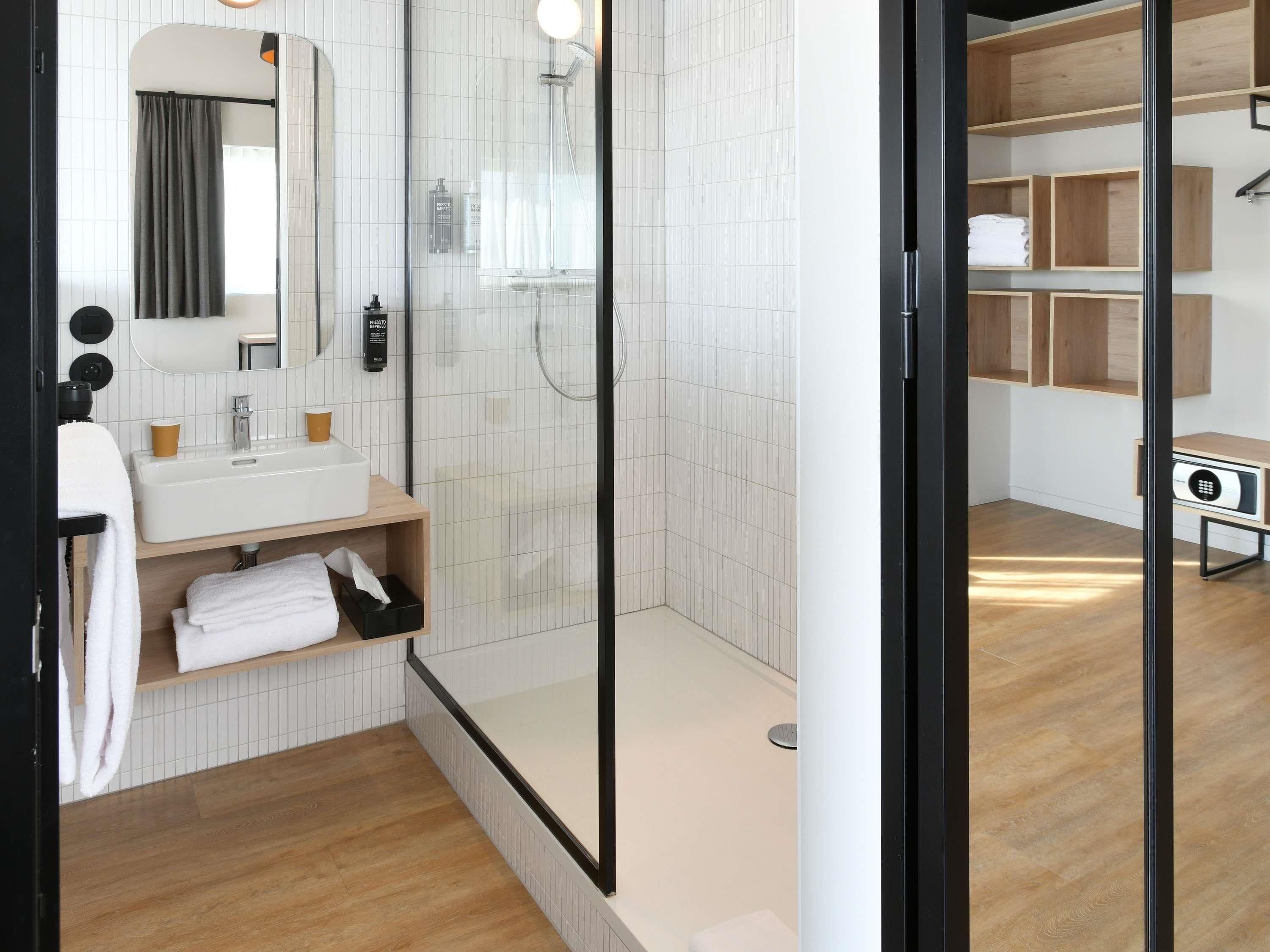 A modern bathroom with a glass-enclosed shower, a white sink with two cups, and a mirror above it.