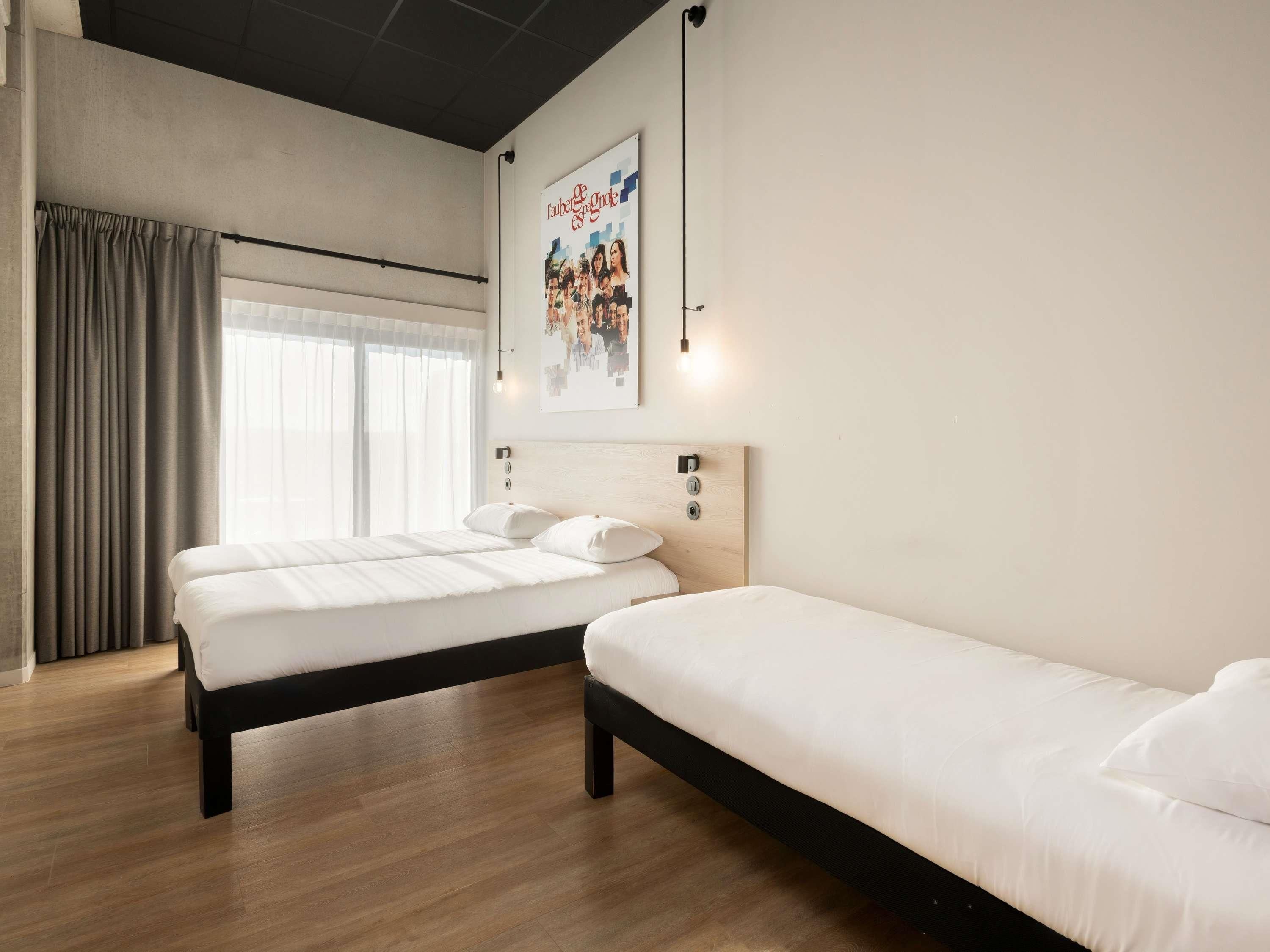 Habitación de hotel con dos camas, un ventanal con cortinas, un cartel en la pared y suelo de madera.