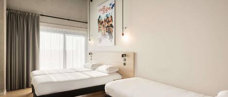 Habitación de hotel con dos camas, un ventanal con cortinas, un cartel en la pared y suelo de madera.