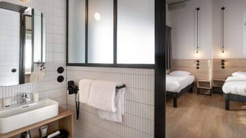 A modern hotel room with a large mirror, a sink, a towel rack, and a bed with a headboard.