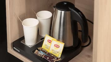 Kahvinkeitin, kaksi paperimukia ja kaksi Liptonin teepussia mustalla alustalla.