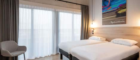Habitación de hotel con dos camas, una silla, un ventanal con cortinas y un cuadro llamativo en la pared.
