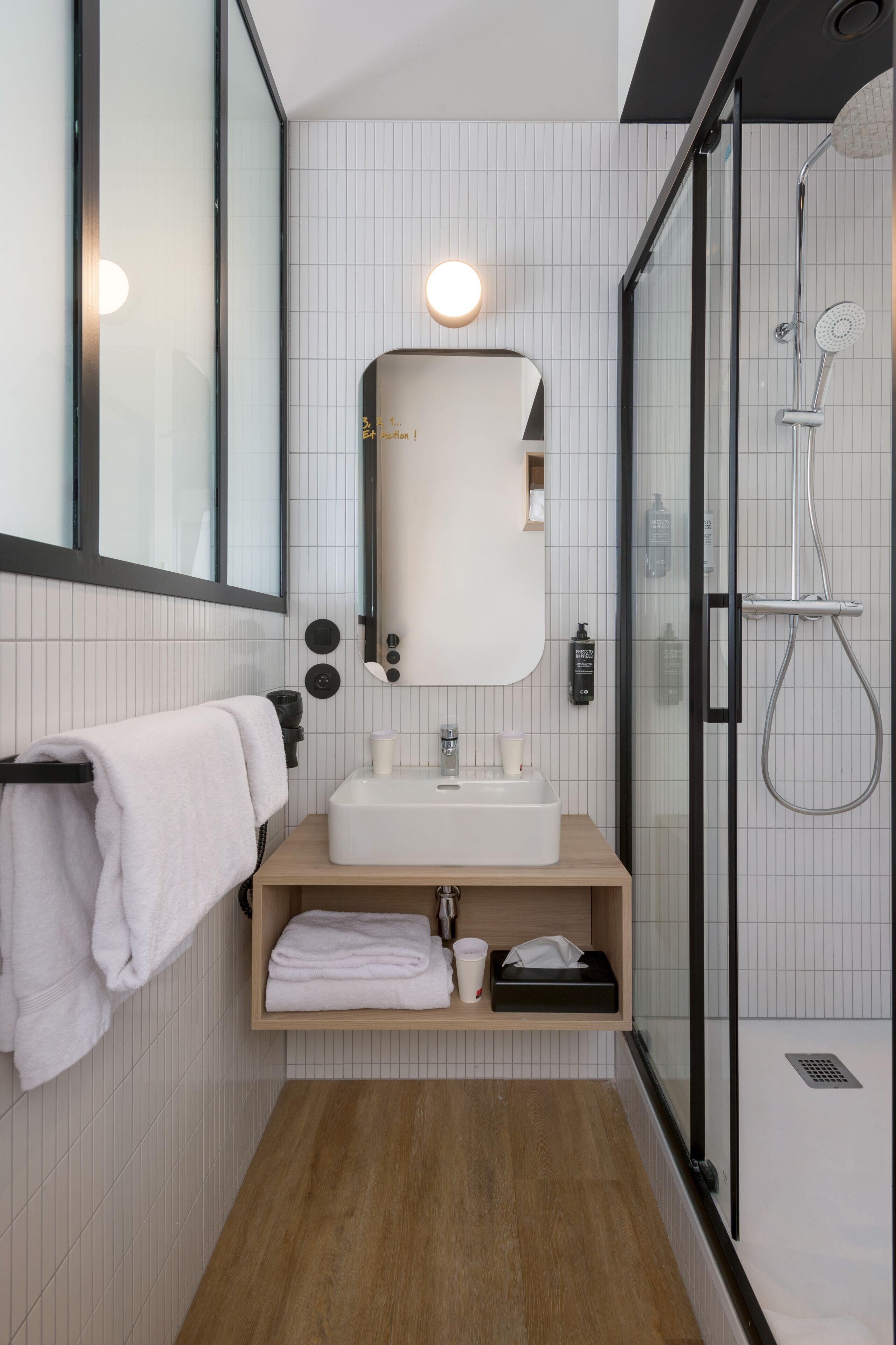 Un bagno moderno con cabina doccia in vetro, lavandino bianco e specchio con luce circolare.