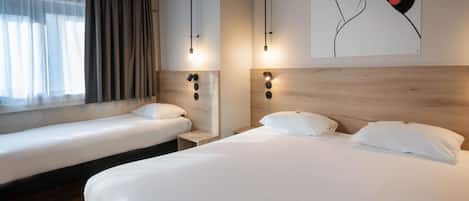 Quarto de hotel com duas camas de solteiro, uma janela grande com cortinas leves e uma obra de arte na parede retratando o rosto de uma mulher com discos de vinil coloridos.