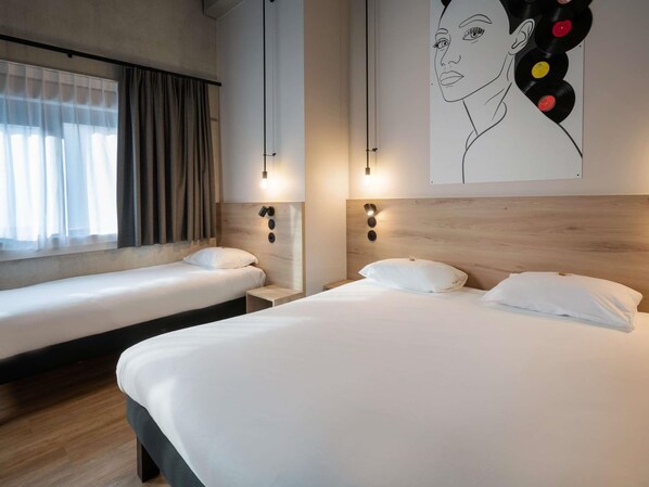 A hotel room with two single beds, a large window with sheer curtains, and a wall-mounted artwork of a woman's face with colorful vinyl records. - Ibis Styles Namur (Namur)