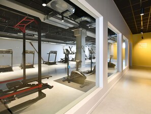 Ein Fitnessraum mit verschiedenen Trainingsgeräten, einer Waage und einem Schild, das den Raum als Fitnessbereich kennzeichnet.
