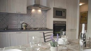 Een moderne keuken met witte kastjes, een gasfornuis, een magnetron en een oven. Er staat een eettafel gedekt met borden, glazen en een vaas met bloemen.