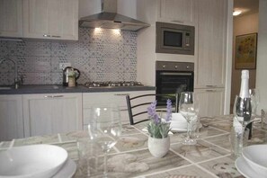 Una cucina moderna con mobili bianchi, piano cottura a gas, forno a microonde e forno. È presente un tavolo da pranzo apparecchiato con piatti, bicchieri e un vaso con fiori.