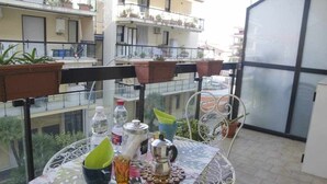 Een balkon met een tafel gedekt voor twee personen, met een metalen stoel, een glazen tafel en potplanten.