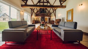 A spacious living room with a high ceiling and exposed wooden beams, furnished with two grey sofas and a wooden coffee table.