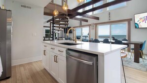 A modern kitchen with a large island, stainless steel appliances, and a view of the ocean.