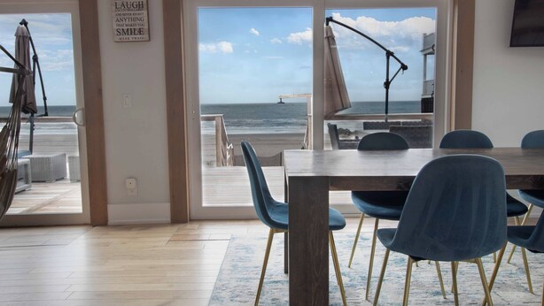 A dining area with a view of the beach, a table, chairs, and a sign with quotes.
