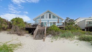 A beachfront house with a wooden staircase leading to a deck.