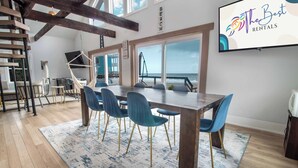 A dining area with a large wooden table, blue chairs, and a view of the ocean.