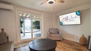 A modern living room with a wooden floor, a round table, a sofa, and a TV mounted on the wall displaying 'The Best Rentals'.