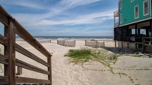 A beach view with a wooden fence, a building with a balcony, and a clear sky.