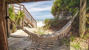 A wooden deck leading to a sandy beach area with a hammock.
