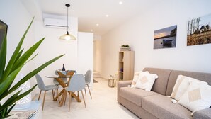 A modern living room with a sofa, dining table, chairs, and a potted plant.