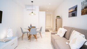 A modern living room with a beige sofa, a dining table with chairs, and a TV on the left.