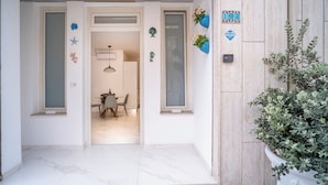 A modern entrance with a glass door, a dining area visible through the door, and a potted plant on the right.