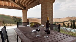A wooden table with two wine glasses and a bottle of wine, set against a scenic hillside view. - VILLA CANTUCCI (Lajatico)