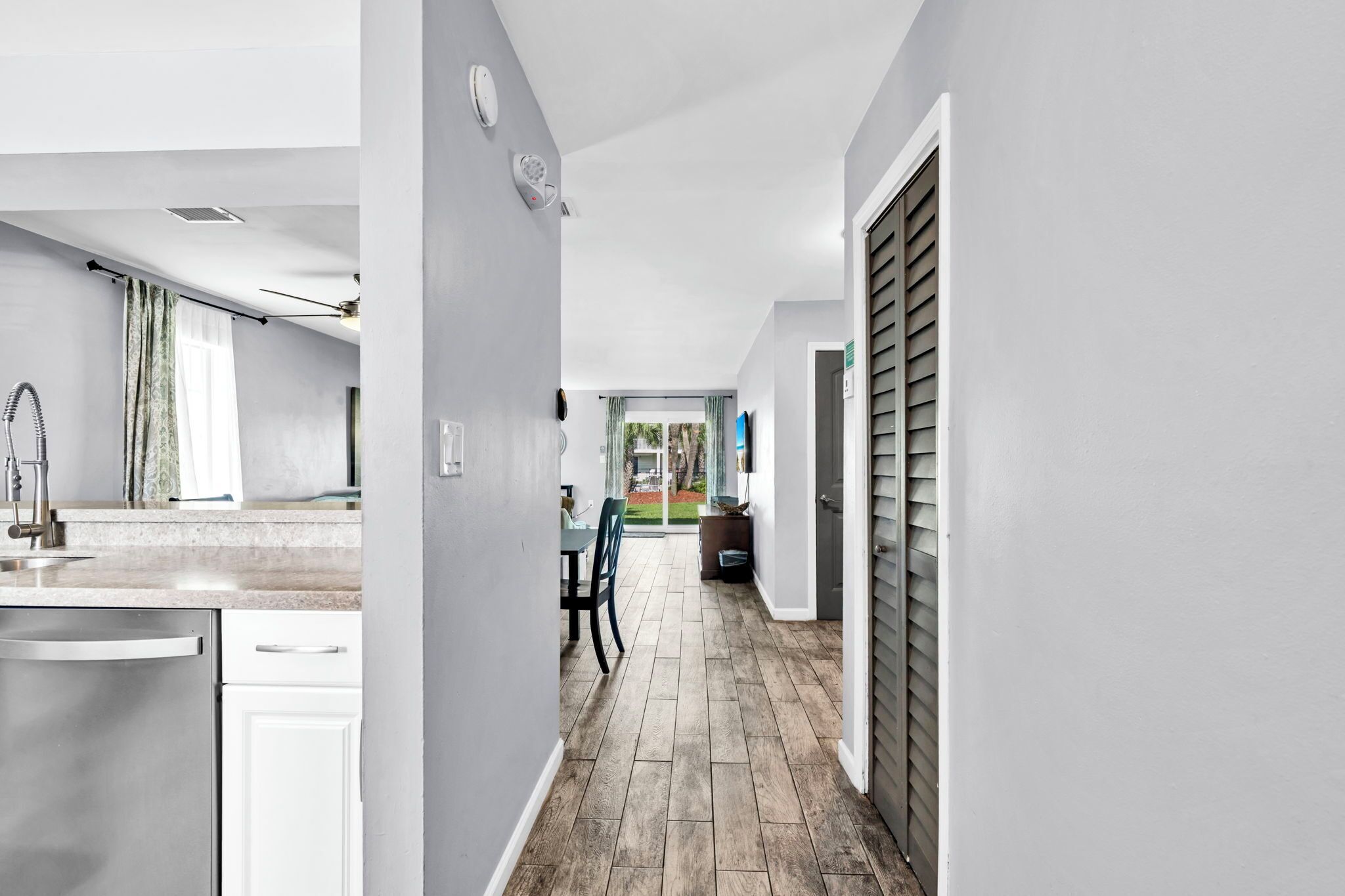 A modern kitchen with white cabinetry and stainless steel appliances, a dining area with a table and chairs, and a hallway leading to a door with a window.