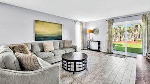 Een moderne woonkamer met een grijze bank, een ronde salontafel en een groot raam met gordijnen.